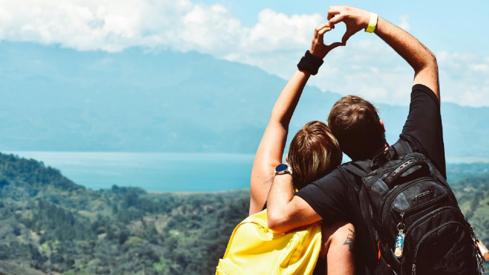 Pareja escalando una montaña, haciendo un corazón con las manos.